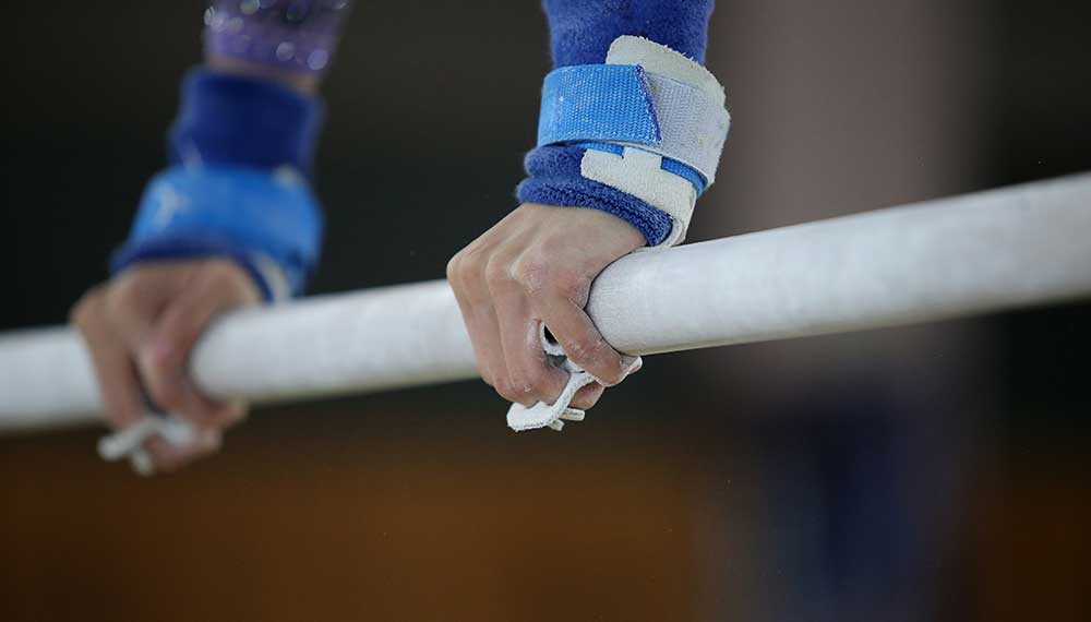 Gymnast gripping the uneven bars during a competition.