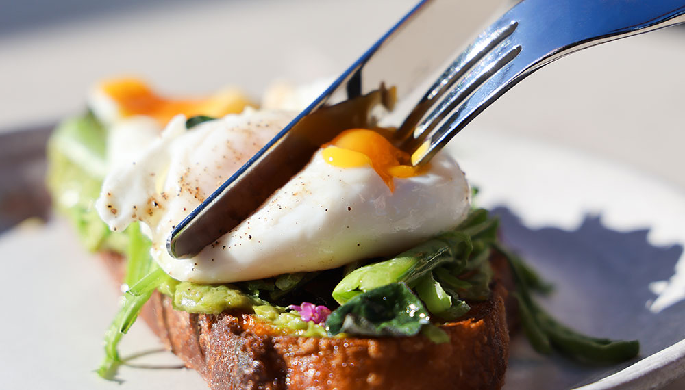 Diner cutting into avocado toast with an egg on top